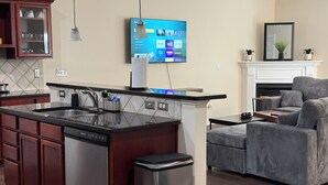 Une cuisine moderne dotée d’un lave-vaisselle encastré, d’un coin repas avec une chaise à revêtement gris et d’un téléviseur à écran plat fixé au mur, qui permet d’accéder aux services de diffusion en continu.