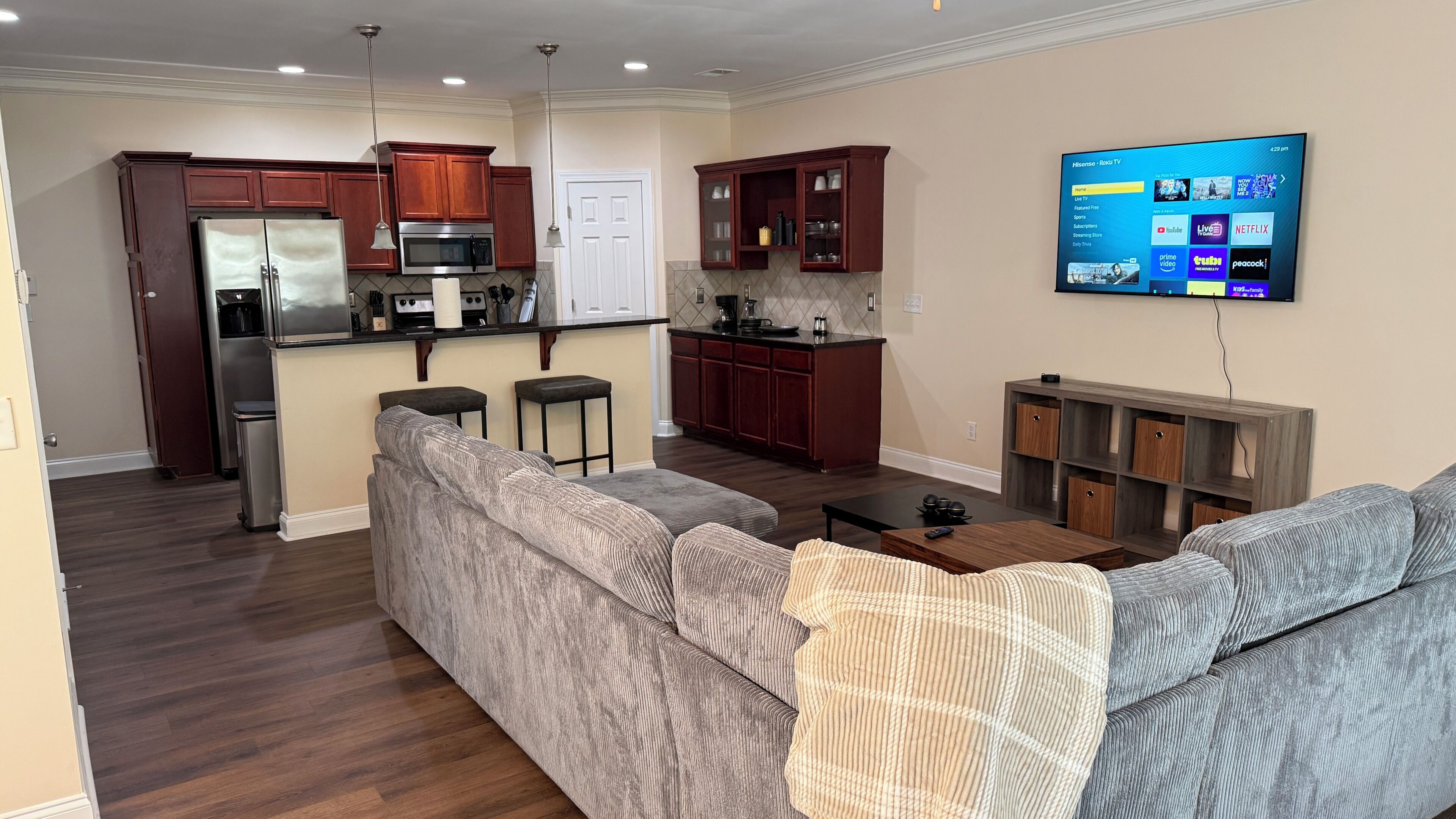 A modern living room with a gray sectional sofa, a small coffee table, and a flat-screen TV mounted on the wall.