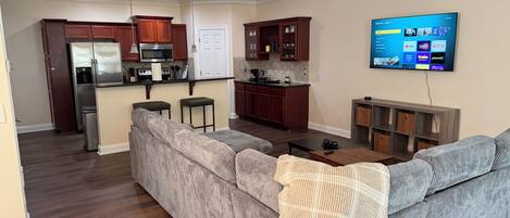 A modern living room with a gray sectional sofa, a small coffee table, and a flat-screen TV mounted on the wall.