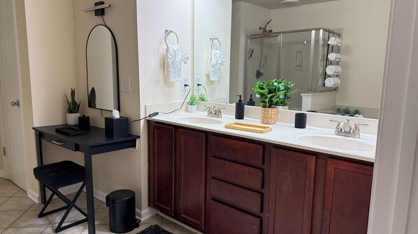 Un baño con lavamanos doble, un espejo, toallero, planta y un cubo de basura.