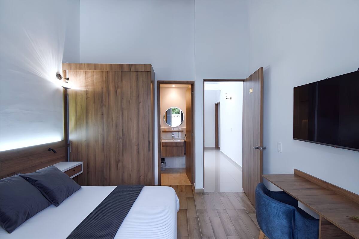 A modern bedroom with a bed, bedside table, wooden wardrobe, and a TV mounted on the wall.