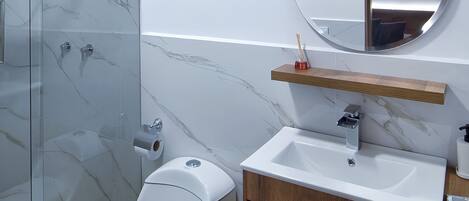 A modern bathroom with a glass shower enclosure, a toilet, a sink with a wooden vanity, and a round mirror.