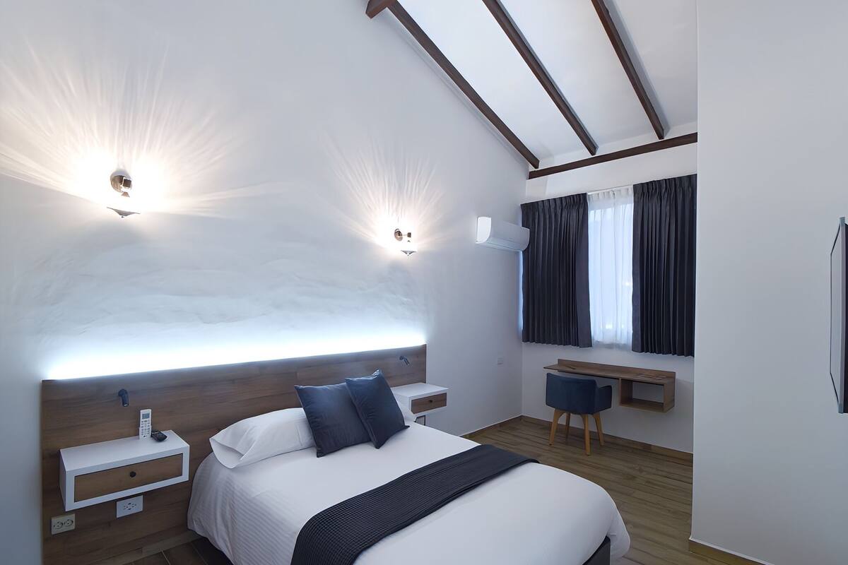 A modern hotel room with a large bed, bedside lamps, a desk, and a window with curtains.