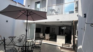 A two-story building with a patio area featuring a table and chairs, an umbrella, and a bench. - Valymar Inn (Cali)