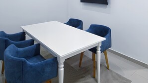 A conference room with a white table, blue chairs, a flat-screen TV on the wall, and a patterned rug. - Valymar Inn (Cali)