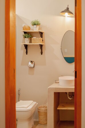 Bany compacte amb vàter, un lavabo i prestatges plens de plantes.