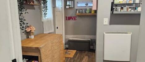 A compact kitchen with a wooden table, a bench, and a shelf with kitchen items.