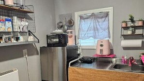 Une cuisine compacte équipée d’un réfrigérateur en acier inoxydable, d’un four à micro-ondes et d’un grille-pain. On y trouve un plan de travail en bois avec un évier, ainsi qu’une fenêtre ornée d’un rideau léger.