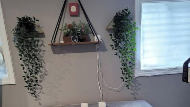 Un bureau en bois, accompagné de deux tabourets blancs rembourrés, d’une plante suspendue et d’une petite étagère sur laquelle se trouvent un haut-parleur et quelques objets décoratifs.