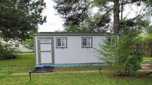 Une petite maison mobile d’un seul étage, avec une porte d’entrée, deux fenêtres et un petit porche.