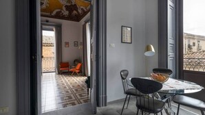 Ein Zimmer mit Essbereich, ein Balkon mit orangenen Stühlen und Blick auf Gebäude.