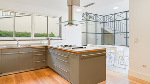 Une cuisine moderne dotée d’un îlot central, d’une grande fenêtre et d’un escalier menant à un niveau supérieur.