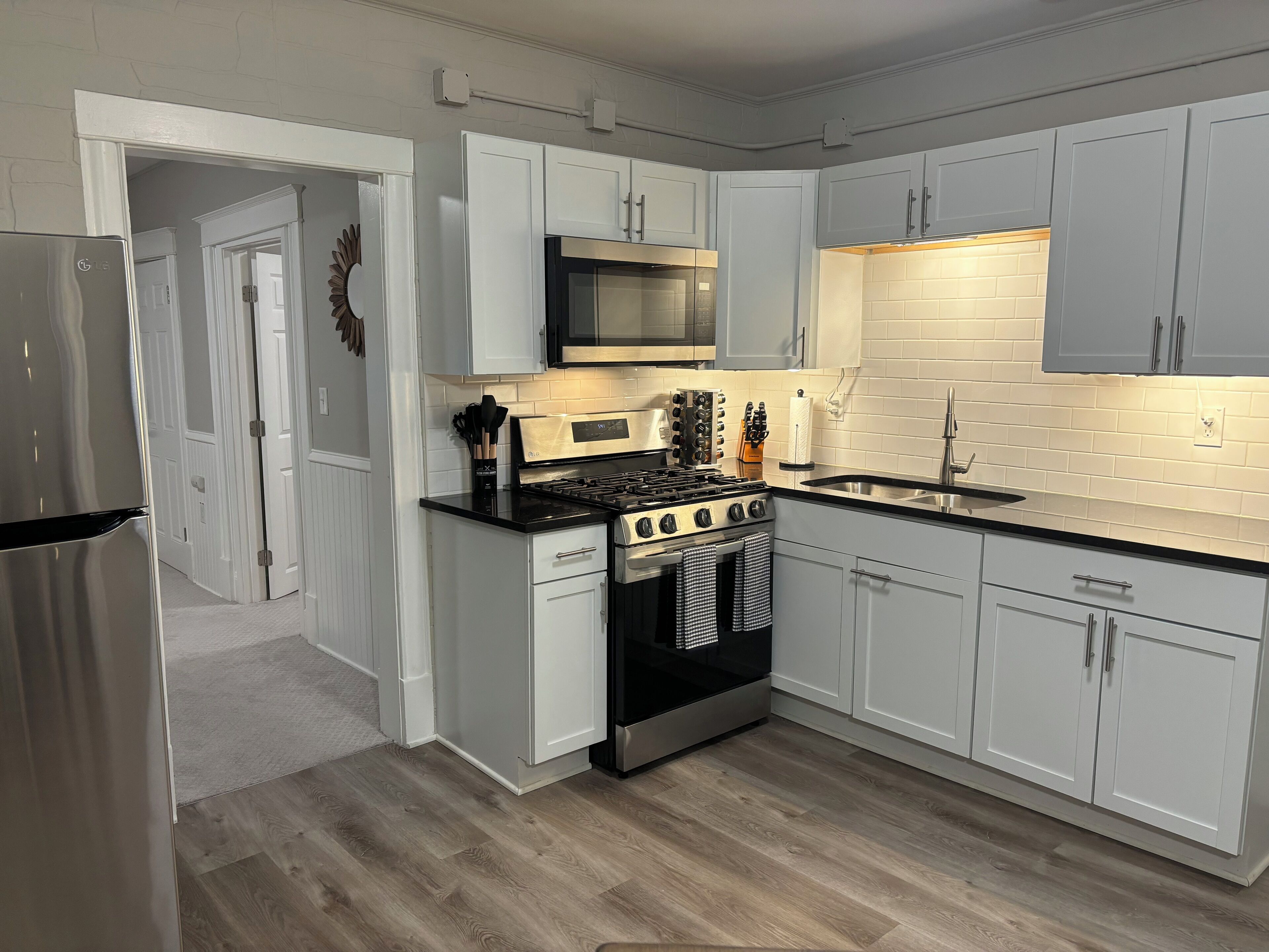 Una cocina moderna con armarios blancos, un refrigerador de acero inoxidable, un microondas, una estufa y un fregadero.