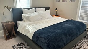 A neatly made bed with a dark blue comforter and white pillows, a bedside lamp, and a patterned rug on the floor.