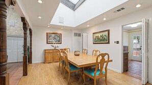 A dining area with a wooden table and chairs, a stone wall, and a skylight. - Charlie IV House at Y.O. Ranch Headquarters - 4-Bedroom Ranch Stay (Mountain Home)