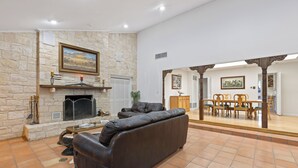 A living room with a stone fireplace, a leather sofa, and a dining area with wooden furniture. - Charlie IV House at Y.O. Ranch Headquarters - 4-Bedroom Ranch Stay (Mountain Home)