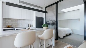 A modern kitchen with white cabinetry, a black refrigerator, and a large window overlooking a cityscape. - Sunlit Sorrento Splendour in Position Perfect (Sorrento)