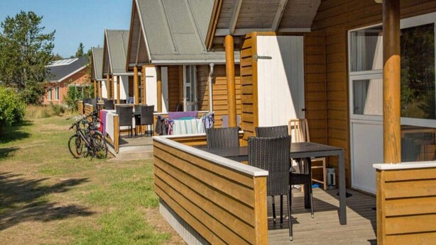 A row of wooden cabins with outdoor seating areas, bicycles, and a grassy yard. - 6 Person Holiday Park Home in Skagen (Skagen)