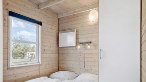 A bedroom with wooden walls, a bed with white bedding, a window with a view of trees, and a wall-mounted heater. - 6 Person Holiday Park Home in Skagen (Skagen)