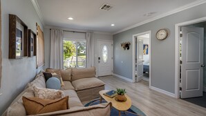 A living room with a beige sectional sofa, a small round table with a plant, and a door leading to another room.