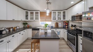 A modern kitchen with white cabinets, a central island, stainless steel appliances, and a window with blinds.