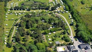 Eine Vogelperspektive zeigt einen Campingplatz mit Wohnmobilen und Reisemobilen, die in einer bogenförmigen Anordnung um eine zentrale Grünfläche angeordnet sind.