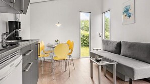 Eine moderne Küche mit Backofen, eine Essecke mit gelben Stühlen, ein graues Sofa und ein großes Fenster mit Blick ins Grüne.