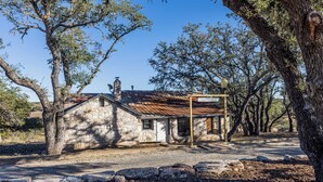 Una casa de pedra rústica amb teulada metàl·lica, envoltada d'arbres.