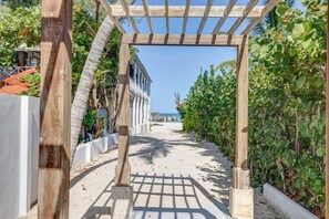 Een strandpad met een houten pergola, omringd door weelderig groen en een helder uitzicht op de oceaan.