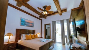 A bedroom with a wooden bed, a ceiling fan, a nightstand with a lamp, a painting on the wall, and a large window with curtains.