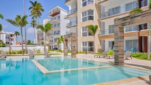 A modern hotel with a pool area, multiple balconies, and palm trees.
