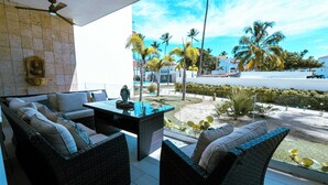 An outdoor seating area with wicker furniture, a glass table, and a view of a pool and palm trees.