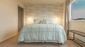 Een slaapkamer met een groot bed, twee hangende lampen, een raam met gordijnen en uitzicht op de omgeving.