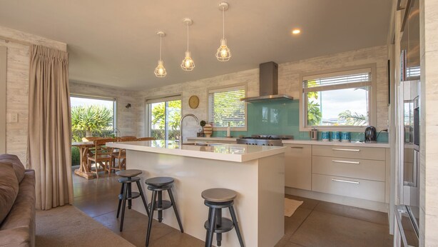 Een moderne keuken met een centraal eiland, barkrukken en hanglampen.
