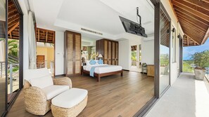 Um quarto espaçoso com uma cama grande, uma TV fixada no teto e uma varanda com móveis de vime.