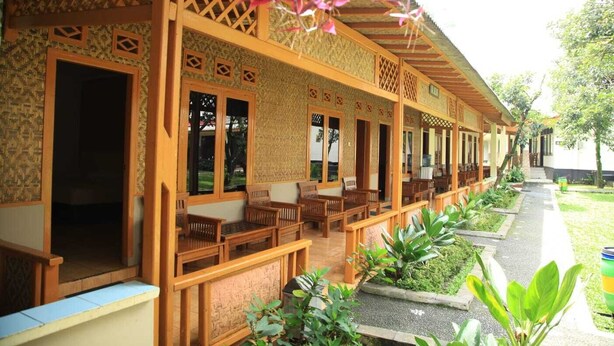 A covered outdoor seating area with wooden furniture and lattice design, surrounded by greenery. - INDRA DJAYA HOTEL (Megamendung)