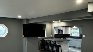 Una sala de estar moderna con un amplio sofá modular, un área de cocina con isla central y un televisor de pantalla plana montado en la pared.