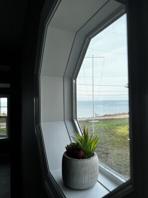 Une fenêtre donnant sur la mer, une plante en pot et un mur blanc.