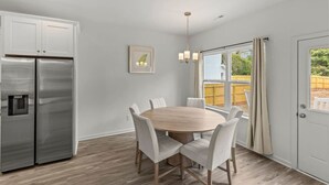 Une cuisine moderne avec un réfrigérateur en acier inoxydable, une table à manger en bois et six chaises, ainsi qu’un luminaire suspendu.