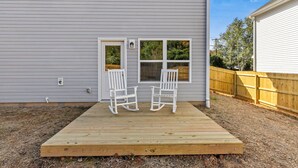 Une maison avec une terrasse en bois, deux fauteuils à bascule et une petite fenêtre.