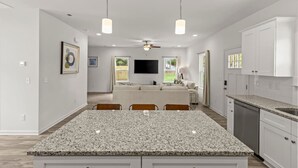 Une cuisine moderne dotée de plans de travail en granit, de meubles blancs et d’un coin repas avec un grand îlot central et des chaises.