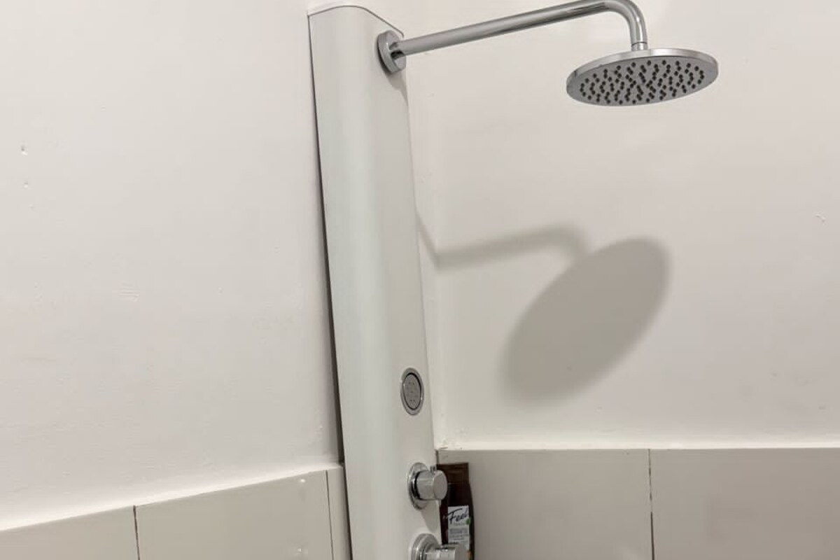 Un box de ducha con cabezal de ducha de mano y panel de control en la pared.