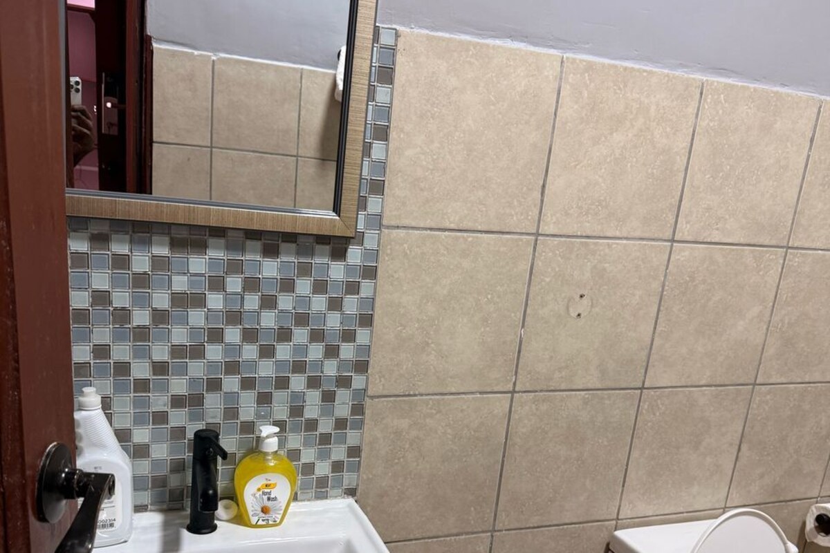 Une salle de bain avec un lavabo blanc, un miroir, des toilettes et un mur recouvert de carreaux.
