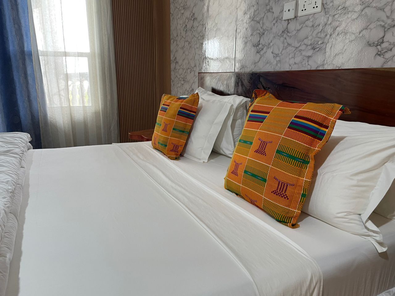 A hotel room with a large bed, white linens, and two colorful pillows.