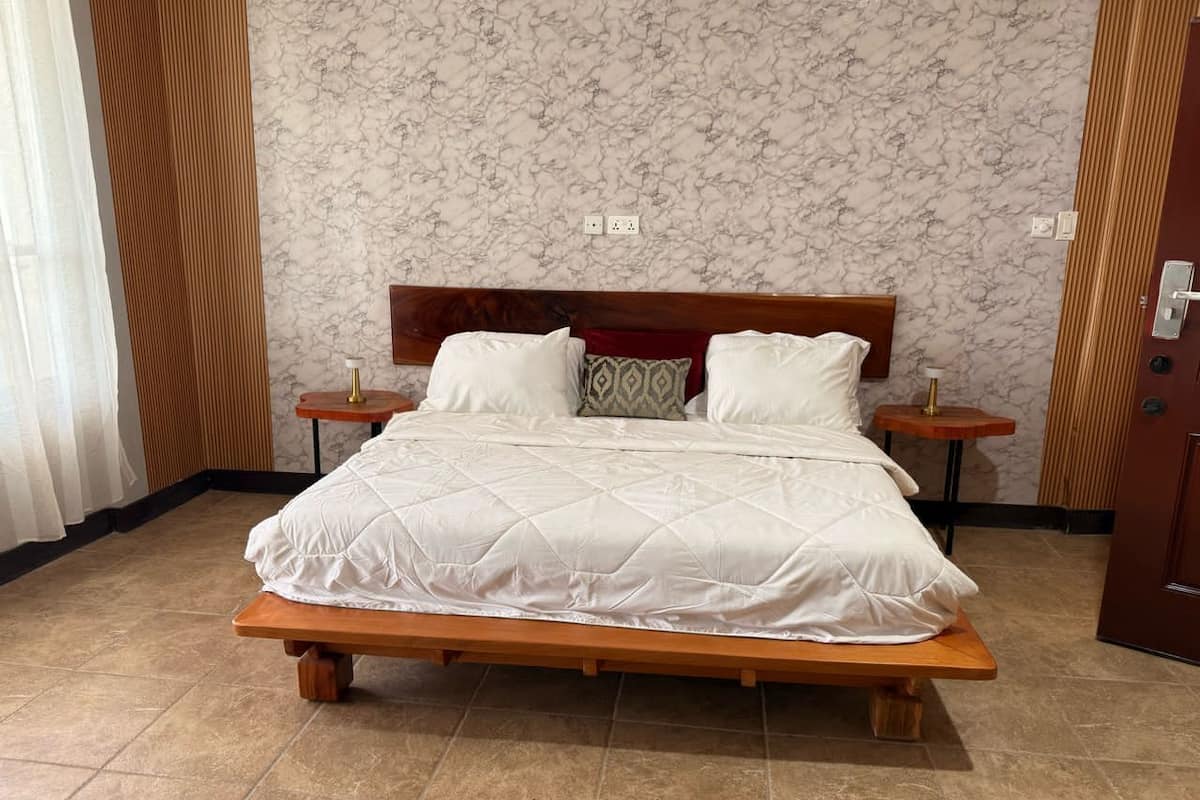 Ein Bett mit Holzrahmen und weißer Bettwäsche, zwei Nachttische mit Lampen und eine Wand mit Marmoroptik.