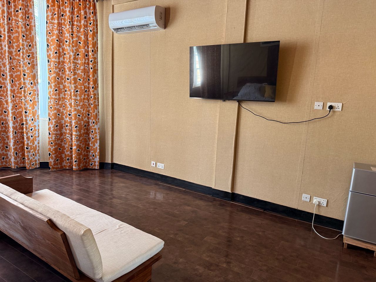 A room with a flat-screen TV mounted on the wall, a wooden bench, and a small cabinet.
