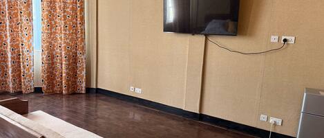 A room with a flat-screen TV mounted on the wall, a wooden bench, and a small cabinet.