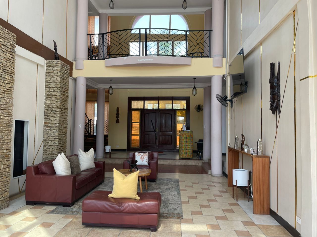 A spacious lobby with a high ceiling, a stone accent wall, a red leather sofa, and a wooden console table.