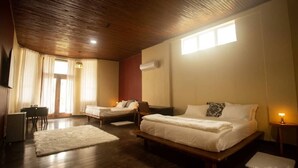 Een hotelkamer met een houten plafond, een groot bed, twee kleinere bedden, een bureau en een stoel.