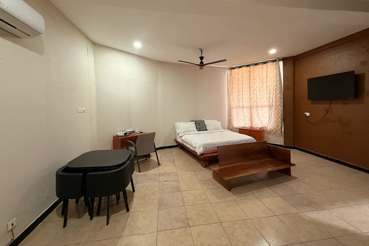 Ein Schlafzimmer mit einem Bett, einem Schreibtisch, einem Sessel, einem Fernseher und einem Deckenventilator.